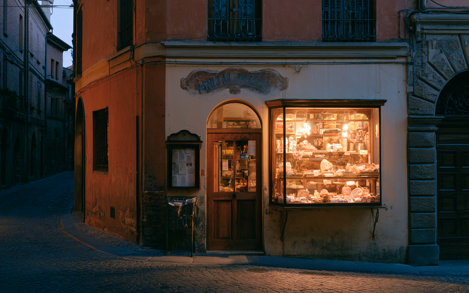 Vetrina di una bottega artigiana italiana al tramonto, luce calda che filtra dalla finestra su una strada acciottolata deserta